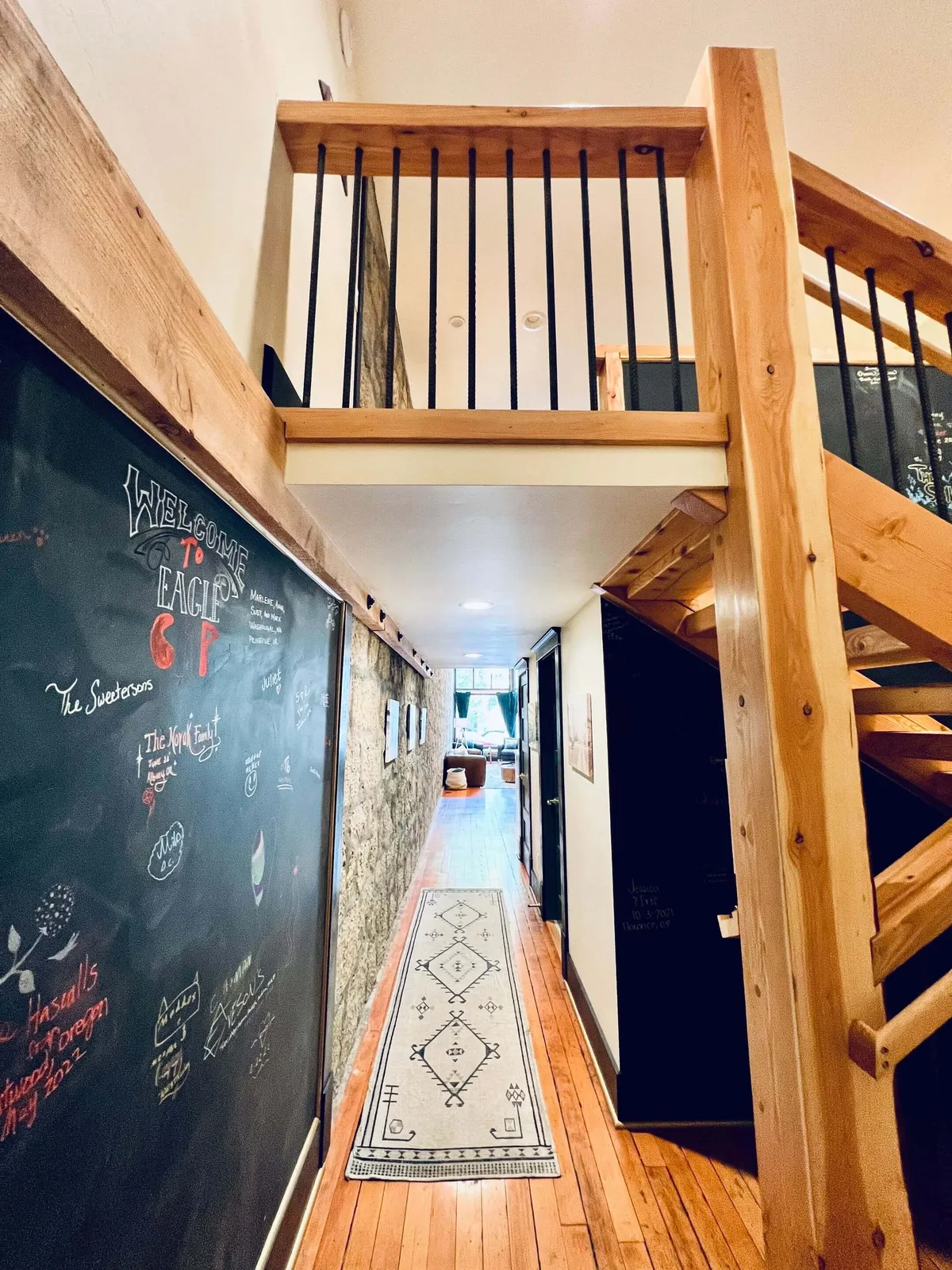 A playful, inviting space anchored by a chalkboard wall with messages, a striking wooden staircase, and a decorative rug. The area exudes a sense of togetherness and artistic expression, suggesting a vibrant environment where families and their pets can bond and create memories.
