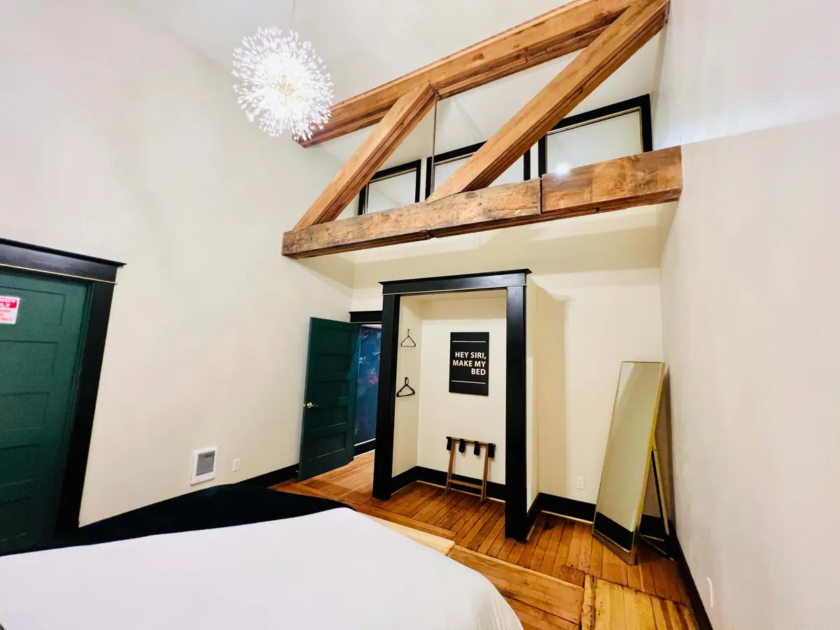 A cozy, modern interior with exposed wooden beams, a stylish light fixture, a large mirror, and wall art featuring text. The comfortable seating and soft lighting evoke both relaxation and an appreciation for art in one's surroundings.