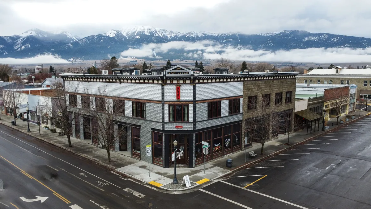 An inviting exterior shot showcasing the historic building's facade set against a picturesque mountain backdrop. The lively street view illustrates people strolling along the sidewalk, exploring local shops, and sampling food at nearby restaurants. The image radiates nostalgic charm, capturing both the scenic beauty and vibrant local activity that defines downtown Enterprise.