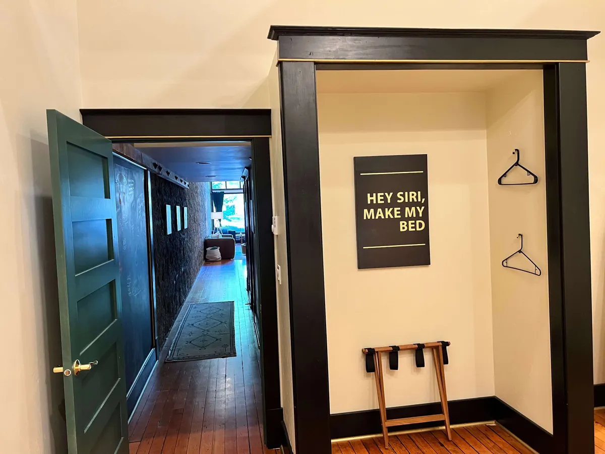 A green door opens into a bright hallway leading to a living area. A coatrack stands ready for guests, and a sign with text sets a friendly, inviting tone. The atmosphere is contemporary, functional, and designed for easy comings and goings—ideal for travelers arriving with pets.
