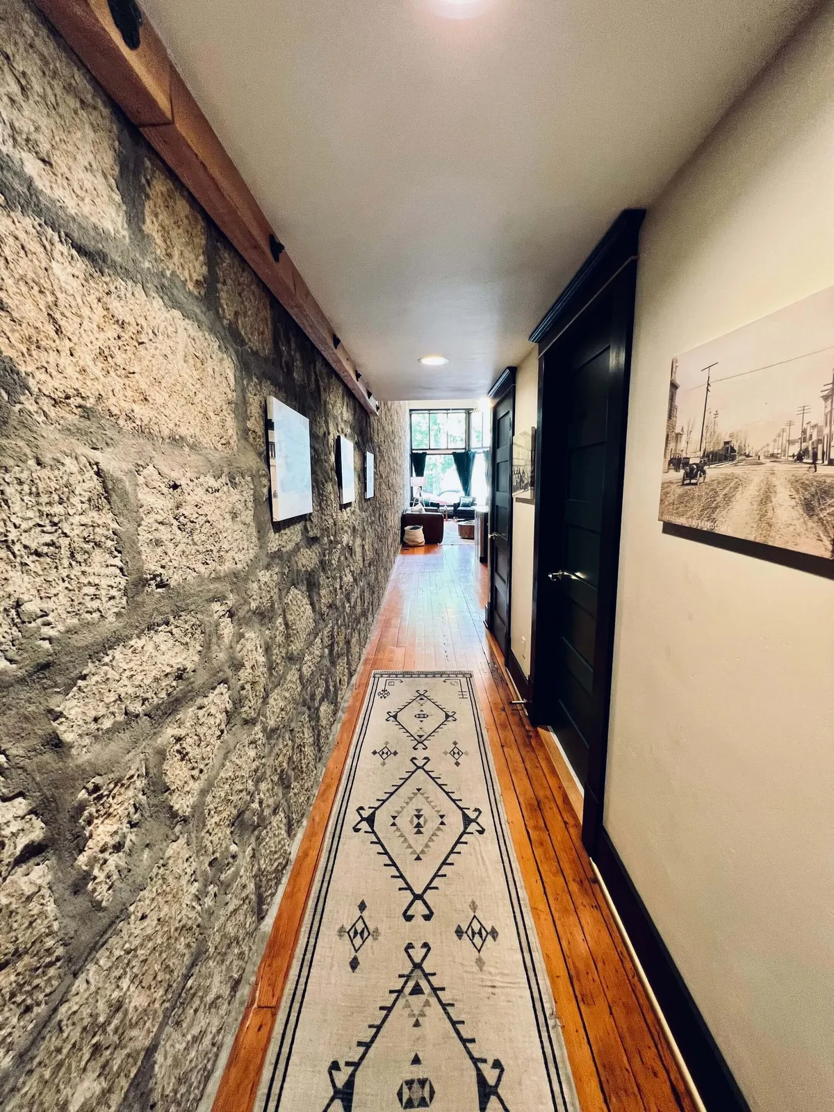 A welcoming entryway or hallway featuring a textured stone wall, vivid decorative rug, and several pieces of distinctive wall art. Glimpses of adjoining rooms and doorways hint at further discovery. The space feels warm and inviting, with evident attention to artistic detail.