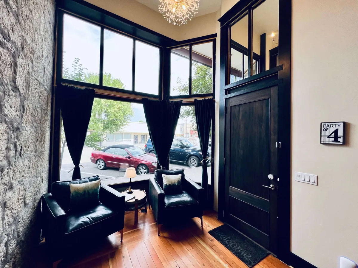 This image displays a bright, open space with large windows letting in natural light, elegant chandeliers, black chairs, and wooden floors. The area is designed for greeting guests, relaxing, or planning the next outing. The welcoming mood and spaciousness suggest a perfect base for regrouping after explorations.