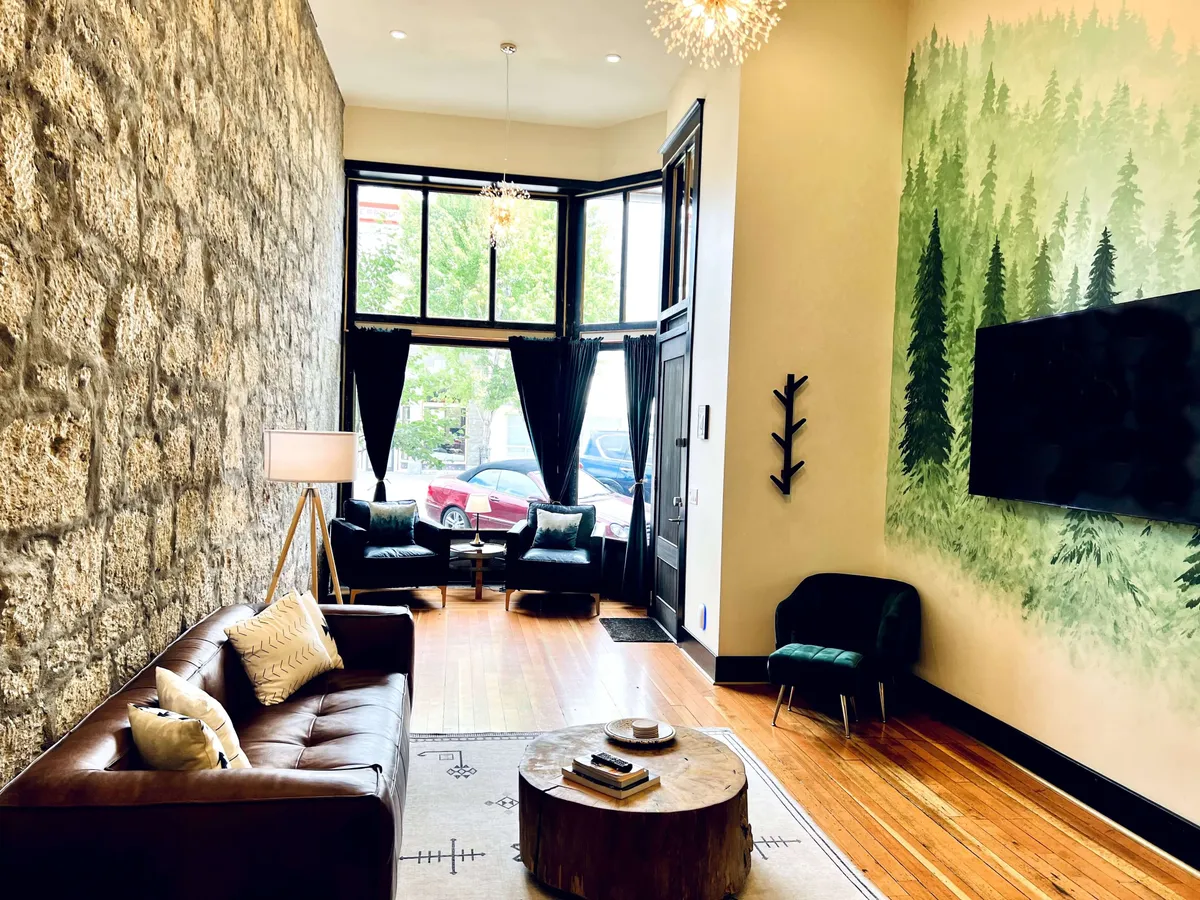 A tranquil living area featuring an impressive stone wall, a green forest mural, a wooden coffee table, and a leather sofa. The ambiance is calm and inviting, ideal for intimate gatherings or quiet relaxation.