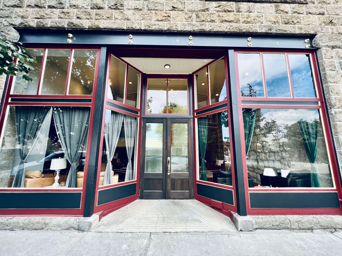 This image captures the exterior of the condo, featuring large glass windows that reflect the surrounding landscape and a detailed wooden door that serves as a welcoming entrance. Soft curtains add a touch of comfort, hinting at the tranquil interior beyond. The overall mood is inviting and hints at a space where guests can relax and reconnect with nature after a day of adventure.