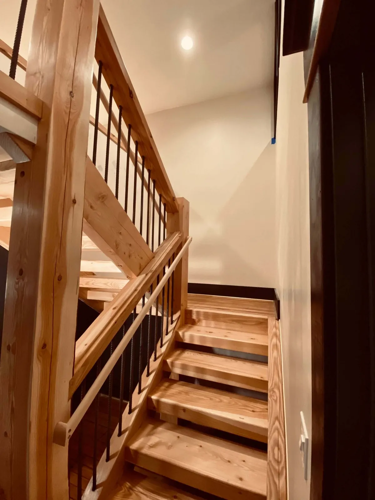 A striking wooden staircase with modern metal railing and a statement light fixture, connecting two levels of the condo. The design encourages movement between shared and private spaces while maintaining a sense of openness and connection.